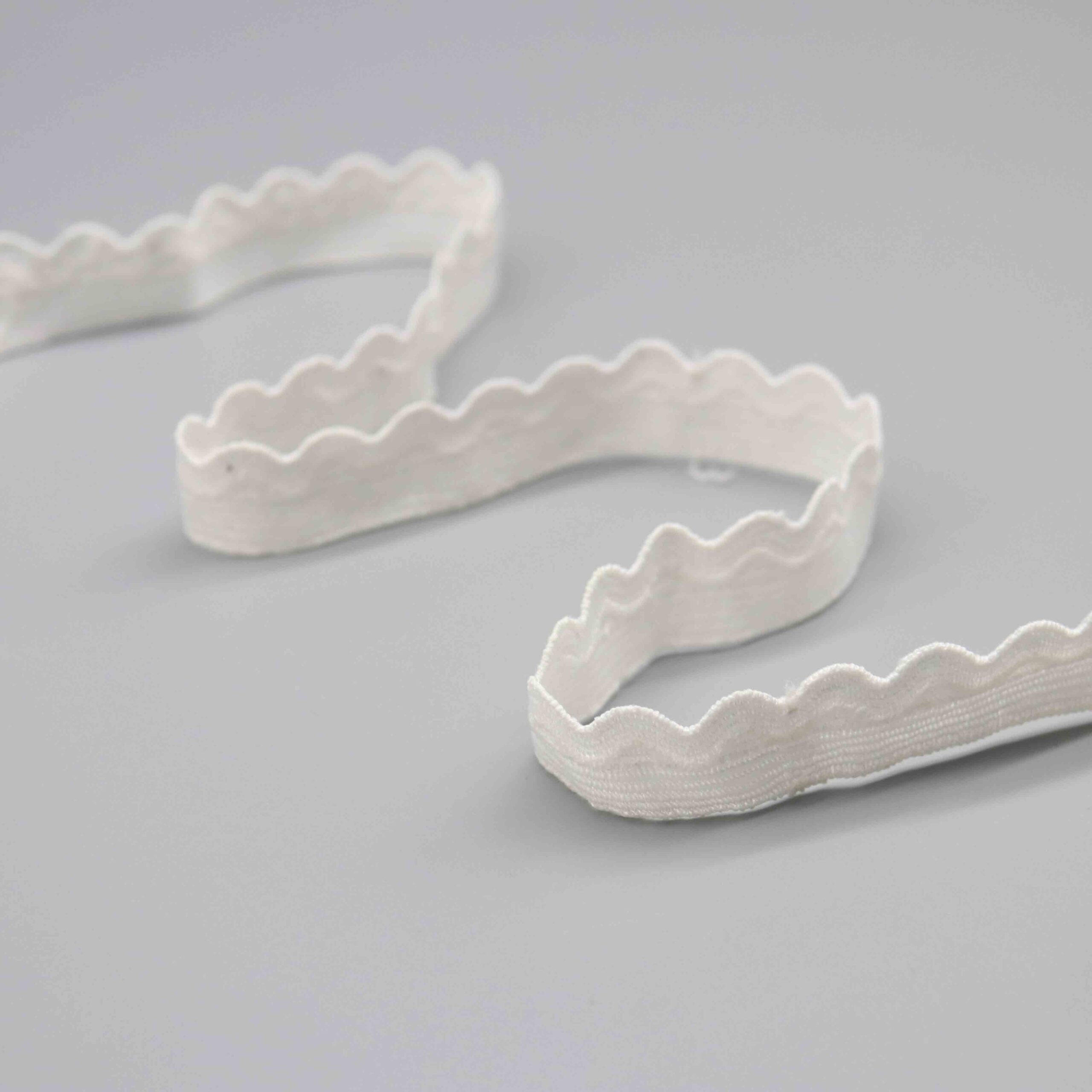 Detailed view of a narrow 2cm white polyester lace trim with classic scalloped edges and streamlined contours for a minimalist aesthetic; water-soluble and softly textured, suited for easy application in clothing decoration, edging, and artistic handmade projects.