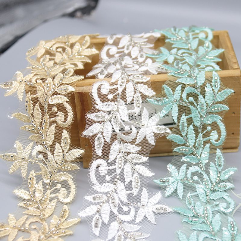 Close-up of gold leaf embroidered lace trim with bead accents, crafted on transparent mesh fabric.