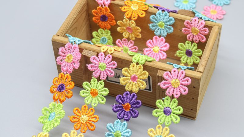 Bright and cheerful water soluble floral lace featuring a variety of daisy colors, suitable for apparel edging and fun home décor ideas.