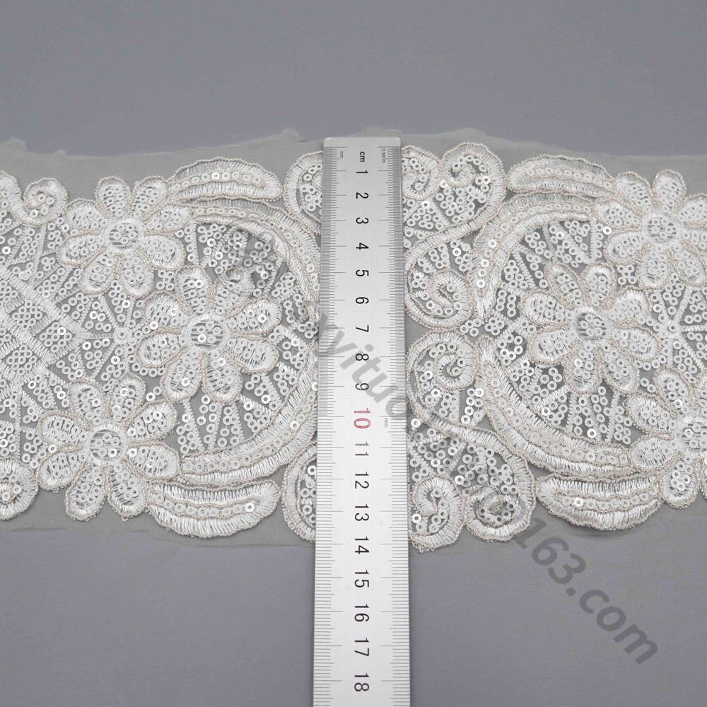 Close-up of wide white lace trim intricately handcrafted with shimmering sequins