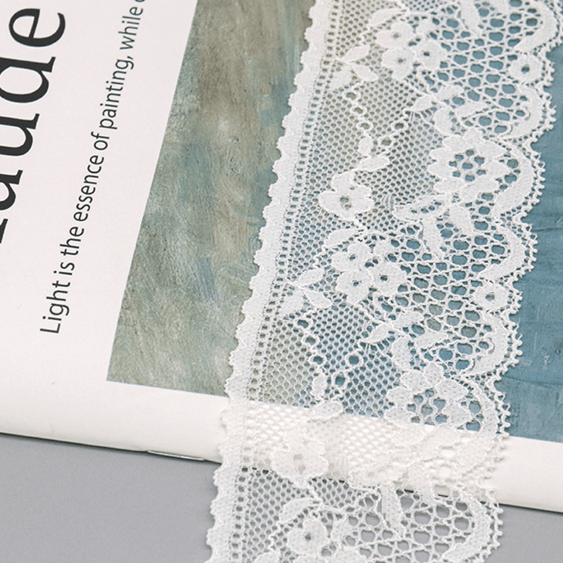 Close-up of a popular white lace trim featuring intricate mesh openwork with layered floral and vine motifs, rounded wave edges with precise lockstitching for a refined finish; soft and lightweight, ideal for adding high-end romance to wedding gowns.