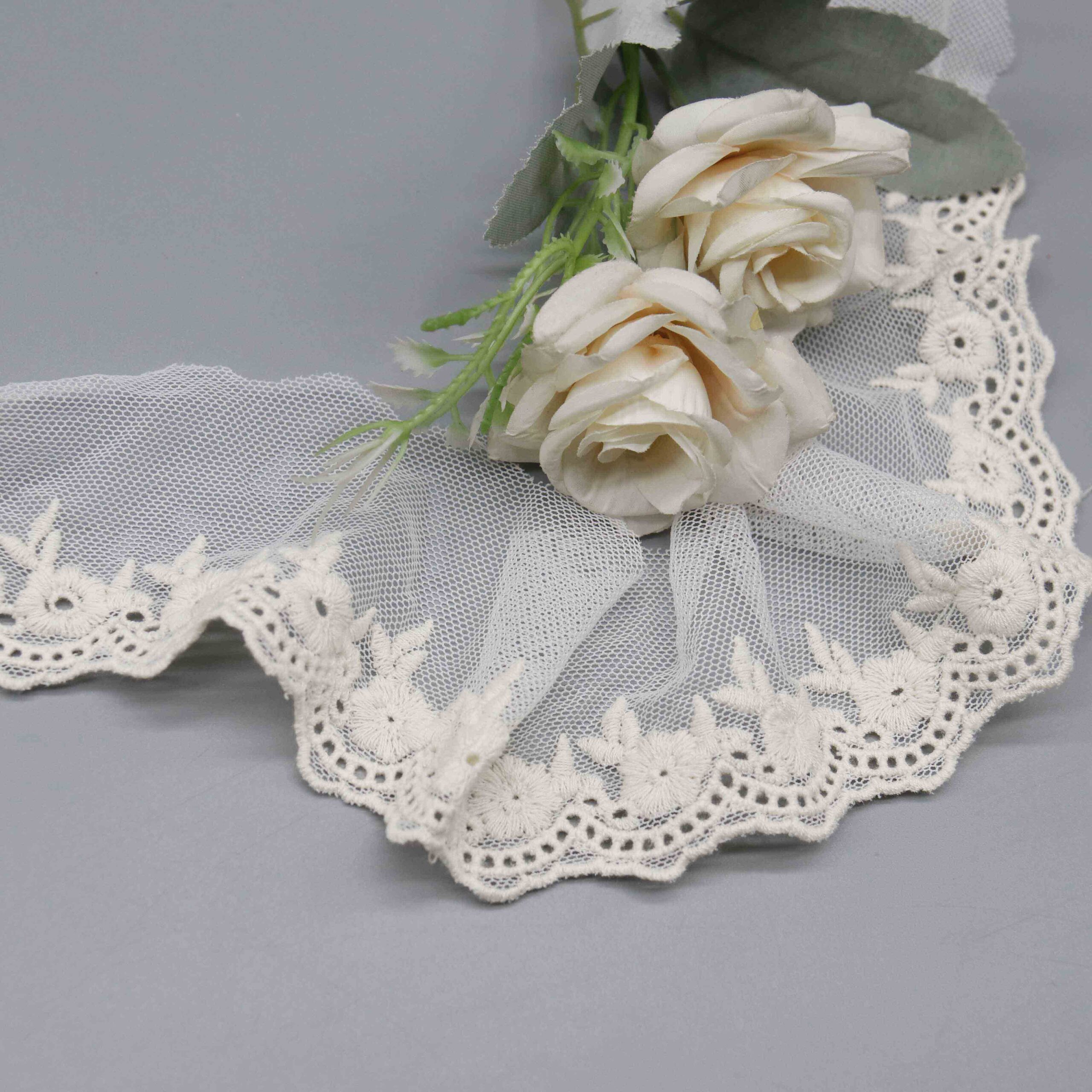 Macro close-up of the daisy petal embroidery with central eyelet holes and leaf spray accents.
