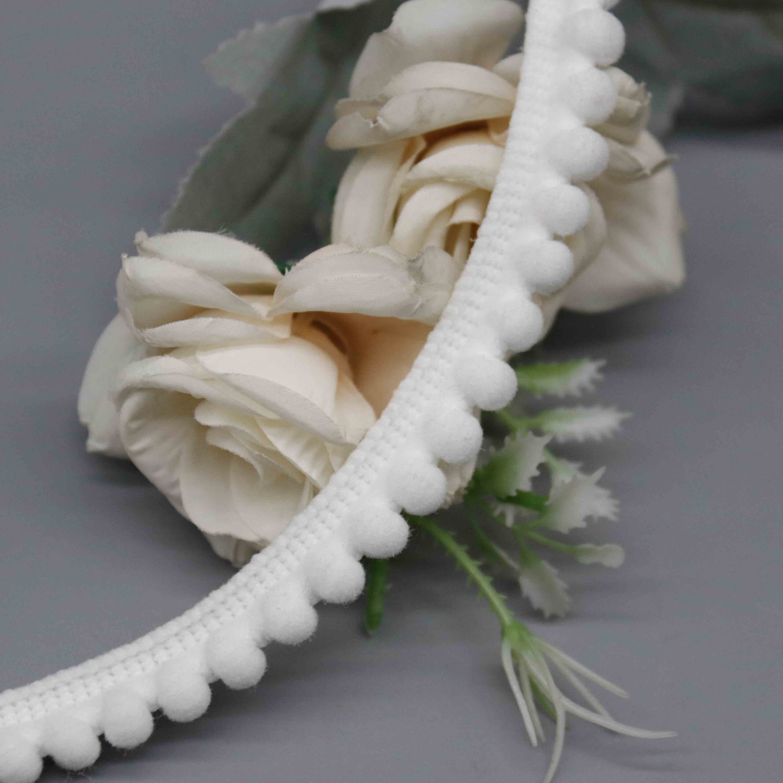 High-resolution detail showing the braided gimp header construction and pompom attachment points.