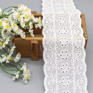 A close-up studio shot of a wide 8cm 100% cotton eyelet lace with a floral medallion pattern and scalloped edges, next to a bouquet of daisies.
