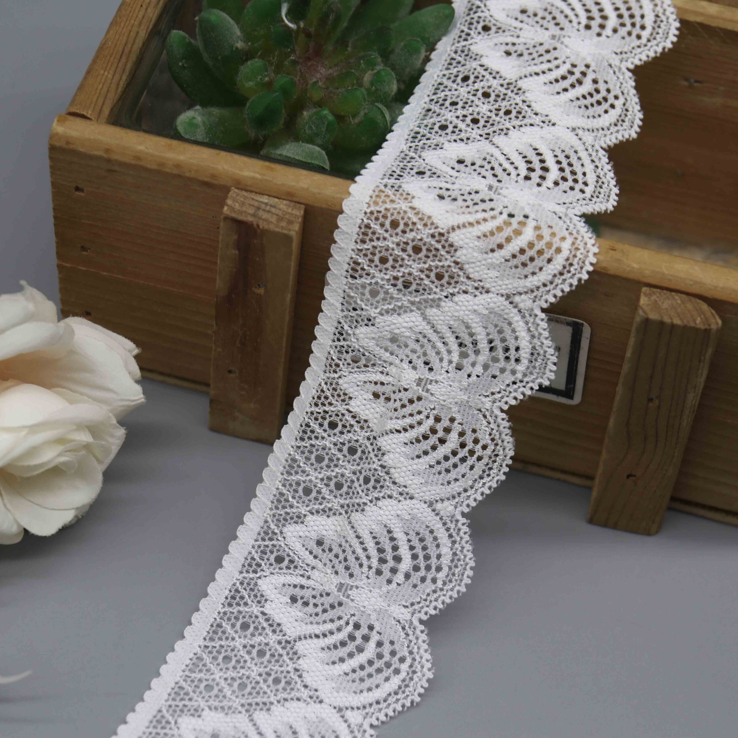 A studio product shot of a 4.6cm wide white scalloped stretch lace trim featuring a distinctive fan pattern, displayed in a wooden box.